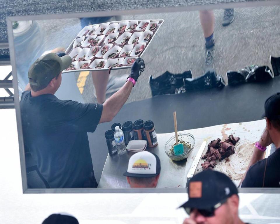 Reflected in the mirror, Jason Baker with Green Mountain Grills takes a tray of bison tenderloin with chimichurri sauce samples over to be handed out to people watching a demonstration by Sterling Smith, right, of Loot N Booty BBQ in Scottsdale, Arizona. The three-day Kansas City BBQ Festival in the parking lot of the GEHA Field at Arrowhead Stadium concluded Sunday, July 11, 2021.