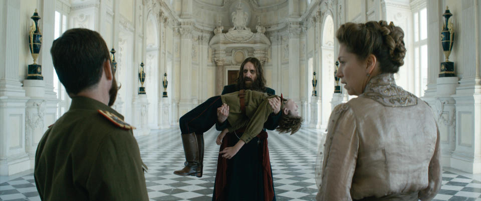 Rhys Ifans as Rasputin (carrying) Alexander Shefler as Tsaravich Alexei, Tom Hollander as Tsar Nicholas (left), Branka Katic as Tsarina Alix (right) in ‘The King’s Man’ - Credit: 20th Century Studios