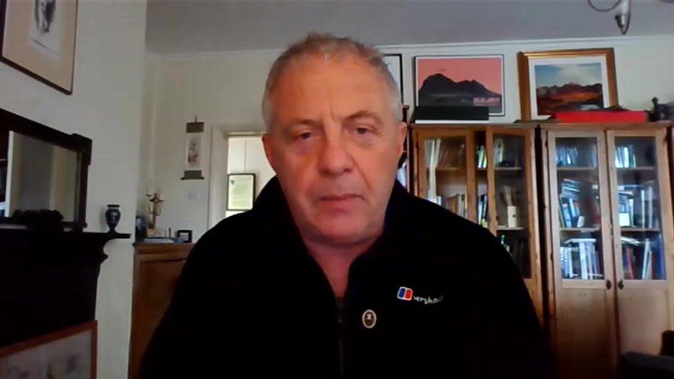 A screenshot image of Lord Mann taken during an interview with the BBC. He is sat in what appears to be a living room, with bookshelves 