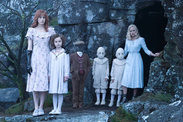 two woman stand at each end of four children as they stand outside a cave