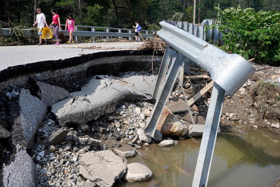 People walk across a bridge damaged by flood waters, Tuesday, July 11, 2023, in Ludlow (AP)