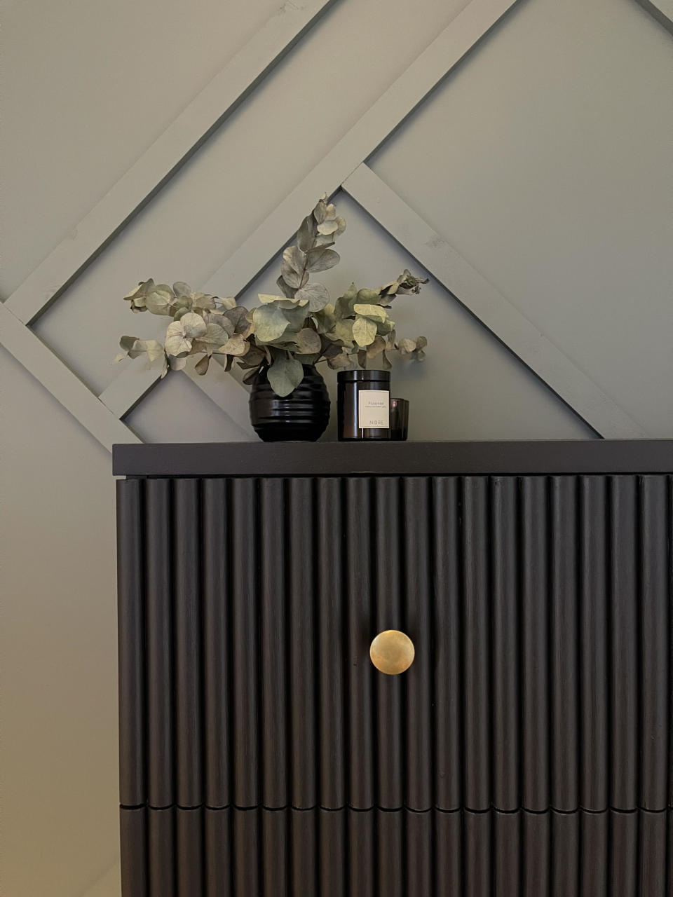 A sideboard in all black, with a fluted exterior and a gold-painted knob