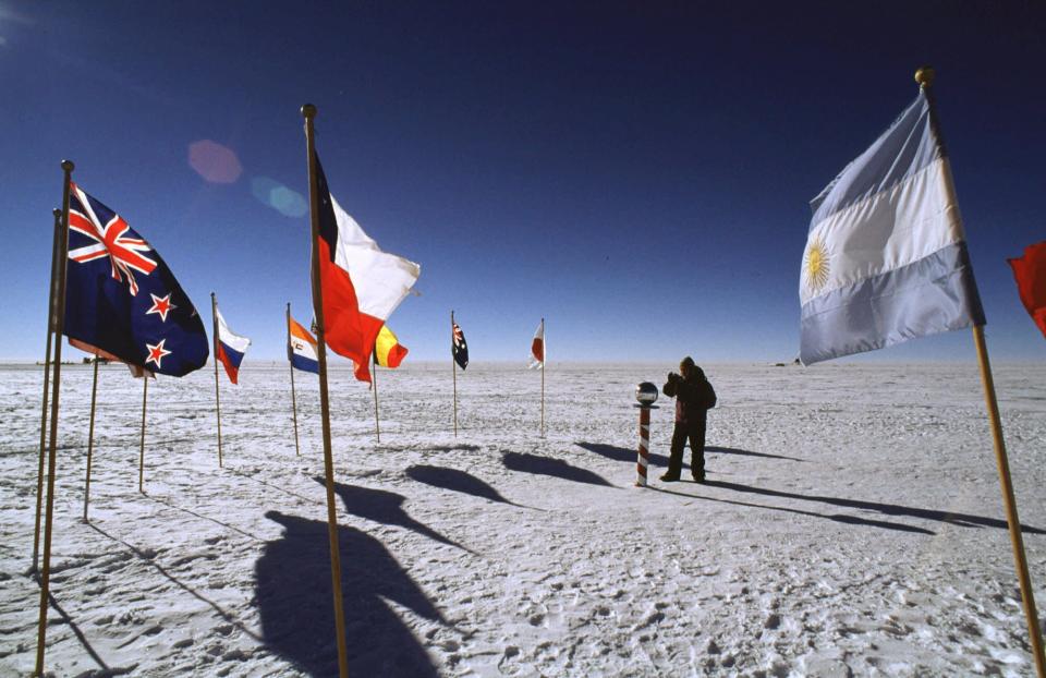 Flags of some of the 43 countries that have signed treaties protecting the South Pole and Antarctica flank the ceremonial marker at the South Pole in December 1997.  A new study released June 29, 2020, said the South Pole is warming at over three times the global rate over the past 30 years.