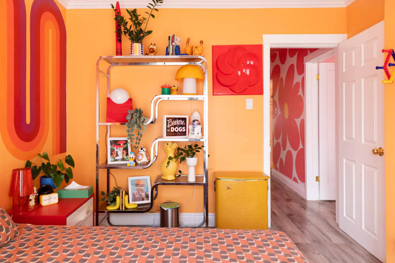 Chrome bookshelf in bedroom with orange painted walls.