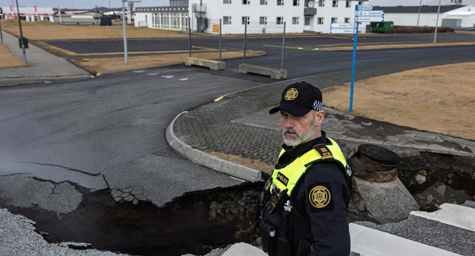 A police officer stands in front of a large crack in the road at Grindavik.