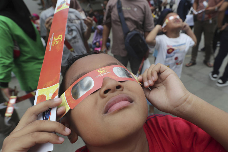 A kid looks up at the sun wearing protective glasses to watch a solar eclipse from Jakarta, Indonesia, Thursday, Dec. 26, 2019. (AP Photo/Tatan Syuflana)