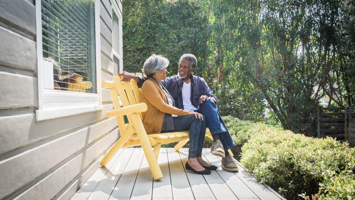 They are sitting on a yellow bench on the decking together outdoors in the garden.