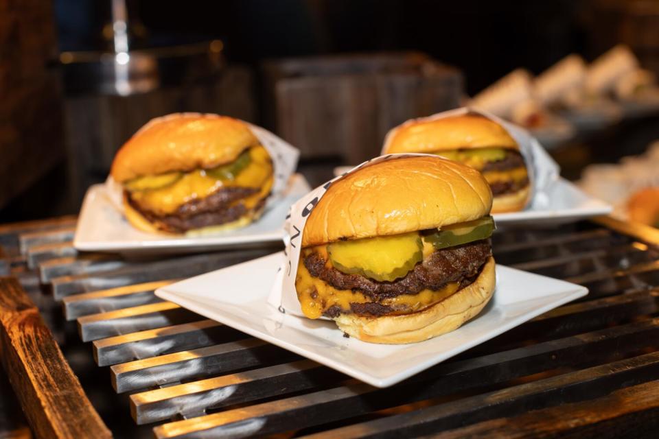 Three double cheeseburgers, each on a square plate, at Intuit Dome