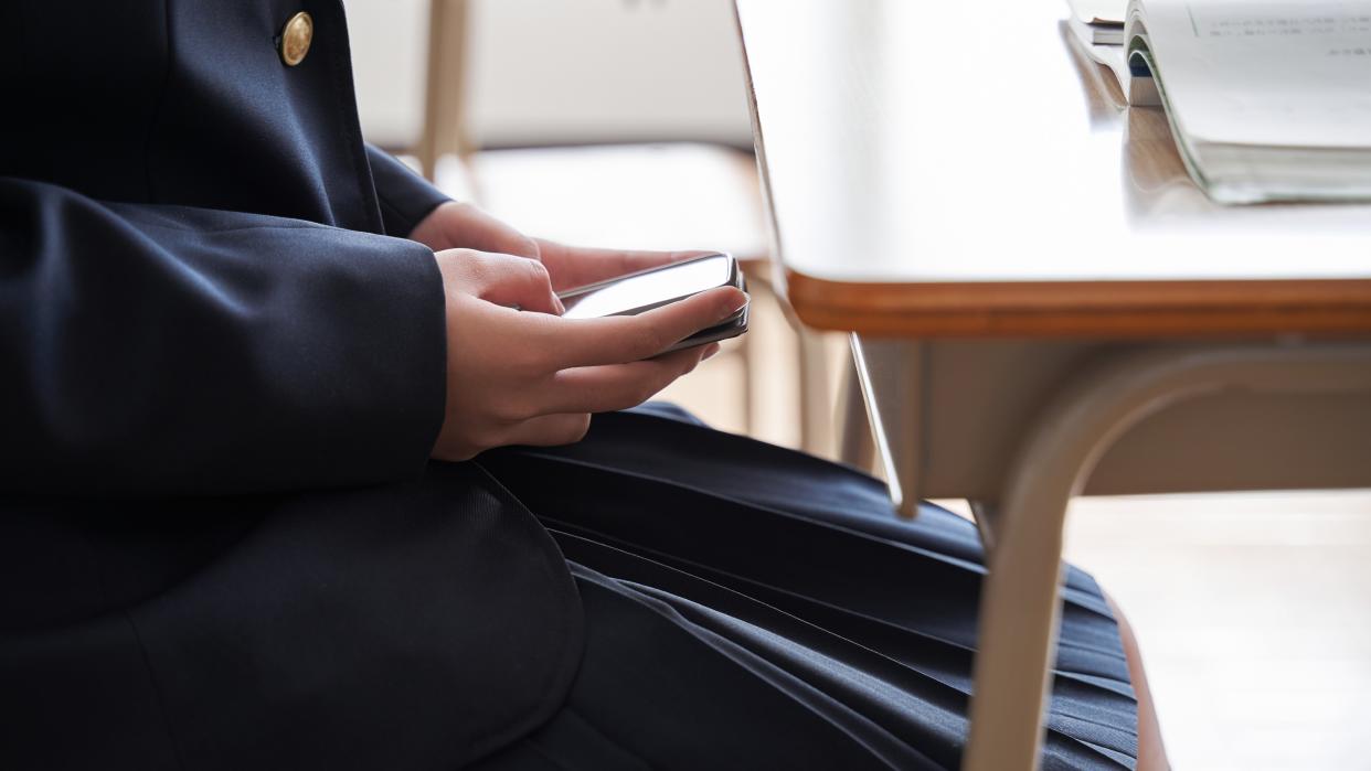  A student hides her cellphone underneath her desk in a classroom. 