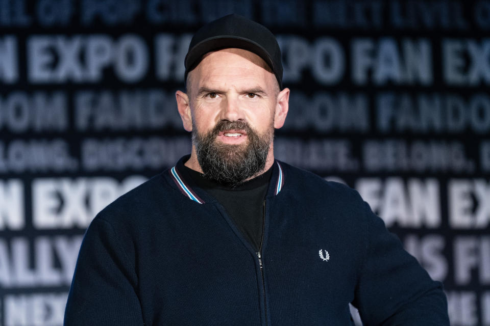 Ethan Suplee poses at a fan expo event. He wears a black cap and a dark jacket