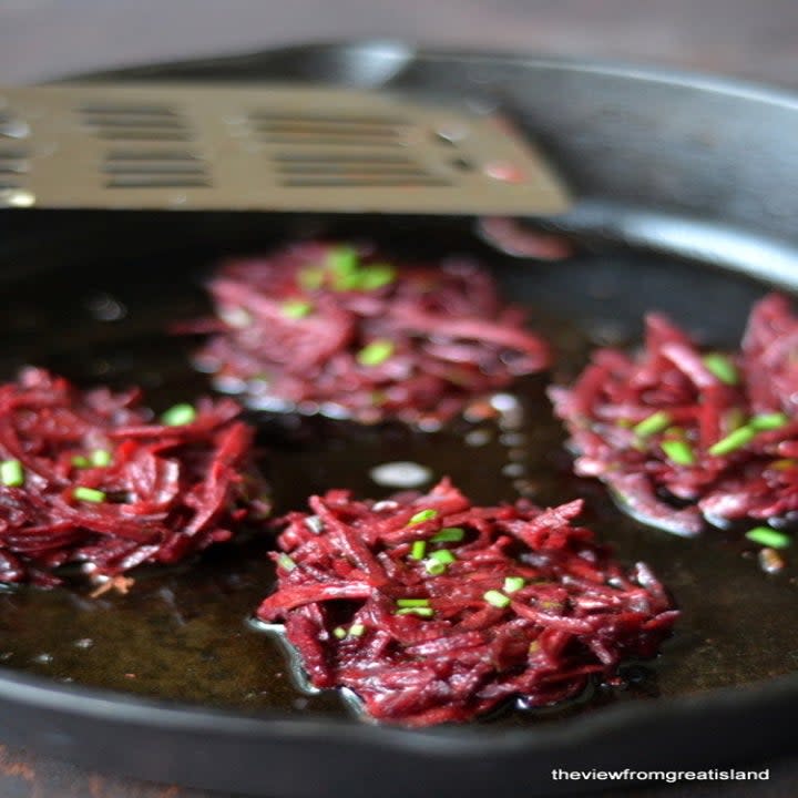 Beet latkes frying in a skillet.