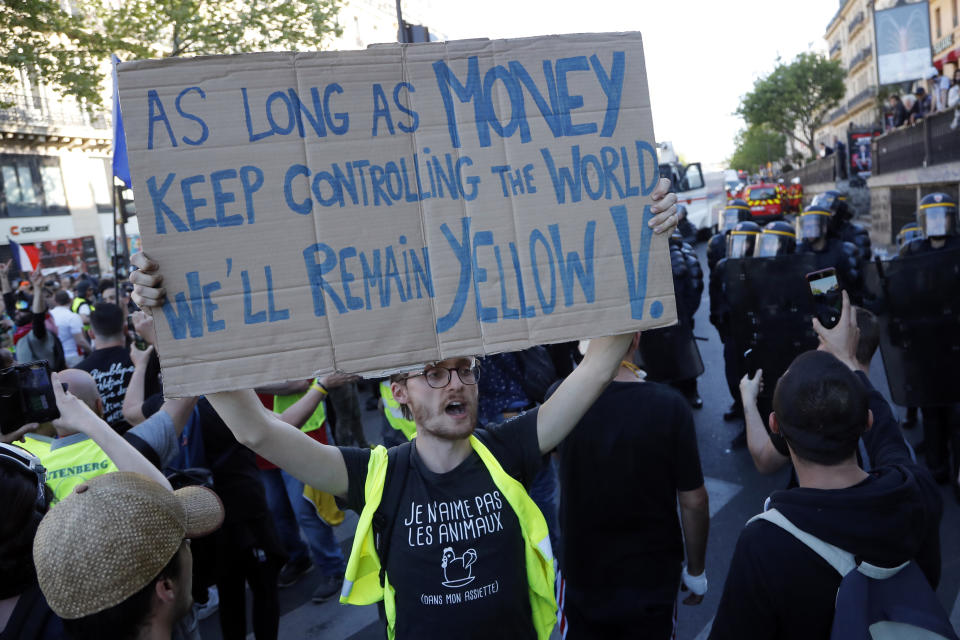 A man in a yellow vest holds up a sign at the Place de Republique during a yellow vest demonstration in Paris, Saturday, April 20, 2019. French yellow vest protesters are marching anew to remind the government that rebuilding the fire-ravaged Notre Dame Cathedral isn't the only problem the nation needs to solve. (AP Photo/Michel Euler)