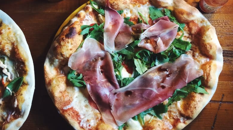 prosciutto arugula pizza on table