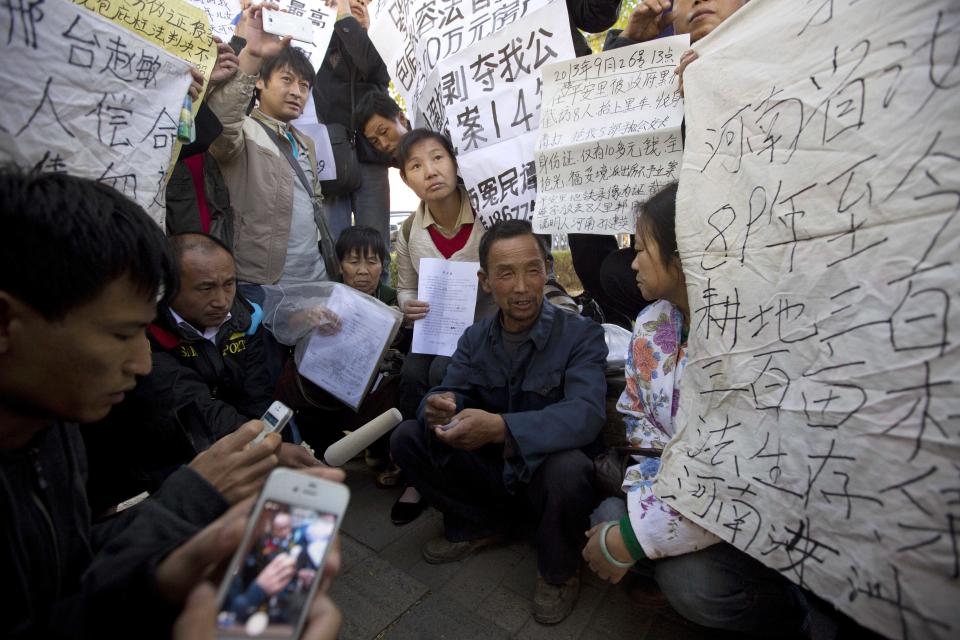 Ji Darong, center, the father of Beijing airport bomber Ji Zhongxing, is surrounded by petitioners trying to catch the media's attention for their own grievances outside the Beijing Chaoyang District Court where Ji Zhongxing faced verdict and sentencing in Beijing, China, Tuesday, Oct. 15, 2013. Ji Zhongxing, a partly paralyzed man who exploded a bomb inside Beijing's airport in hopes of winning redress over an alleged beating by public officials, was given a six-year prison sentence Tuesday. (AP Photo/Ng Han Guan)