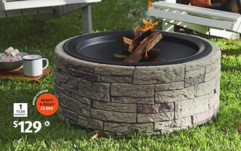 Aldi fire pit sits on a lawn surrounded by furniture and picnic items.