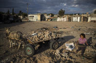 A Palestinian girl walks next to a donkey carte loaded with rocks in a slum on the outskirts of Khan Younis Refugee Camp, in the southern Gaza Strip, Wednesday, Nov. 25, 2020. Israel's blockade of the Hamas-ruled Gaza Strip has cost the seaside territory as much as $16.7 billion in economic losses and caused its poverty and unemployment rates to skyrocket, a U.N. report said Wednesday, as it called on Israel to lift the 13-year closure. (AP Photo/Khalil Hamra)