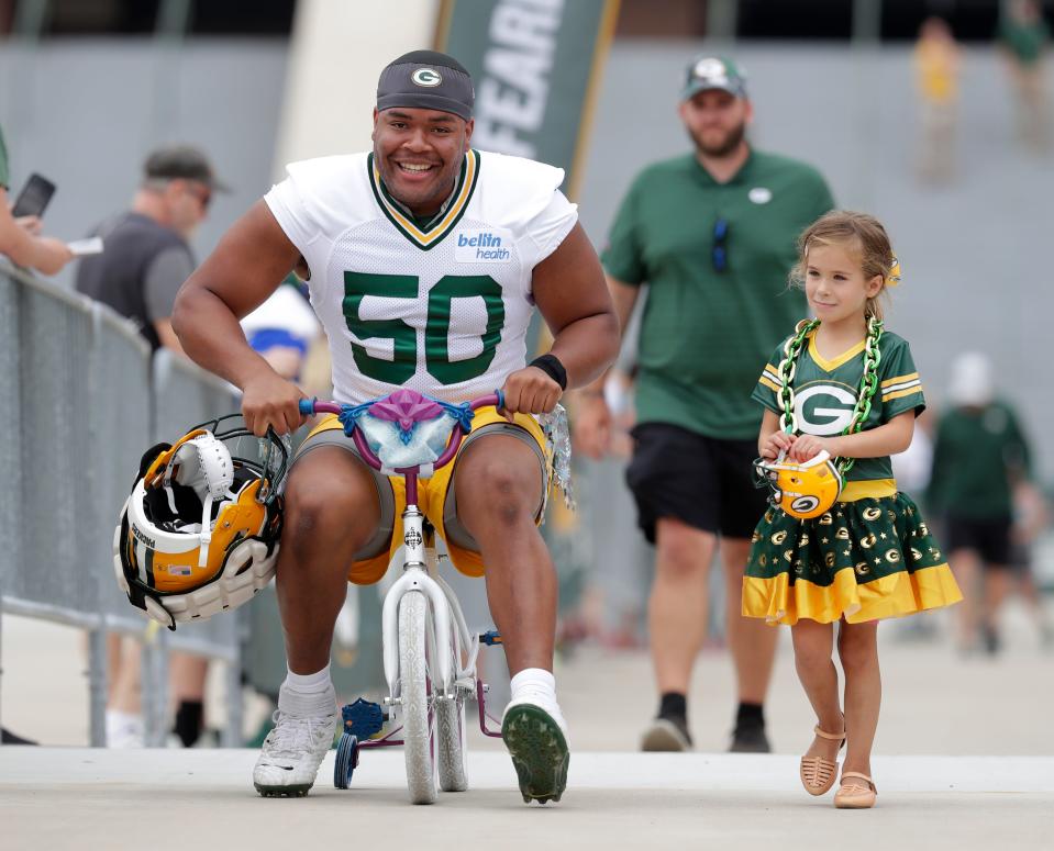 Green Bay Packers offensive lineman Zach Tom (50) rides the bike of a young Packers fan in the Green Bay Packers DreamDrive on the first day of the 2022 training camp in Green Bay.