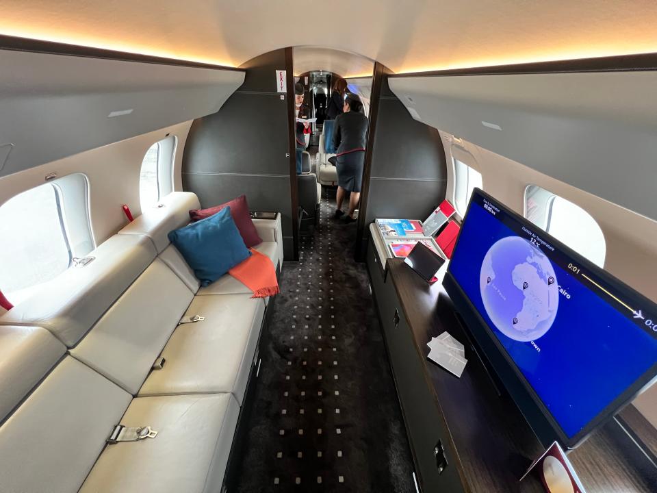 The television / living area of a VistaJet Bombardier Global 7500 with a long sofa and cushions and literature