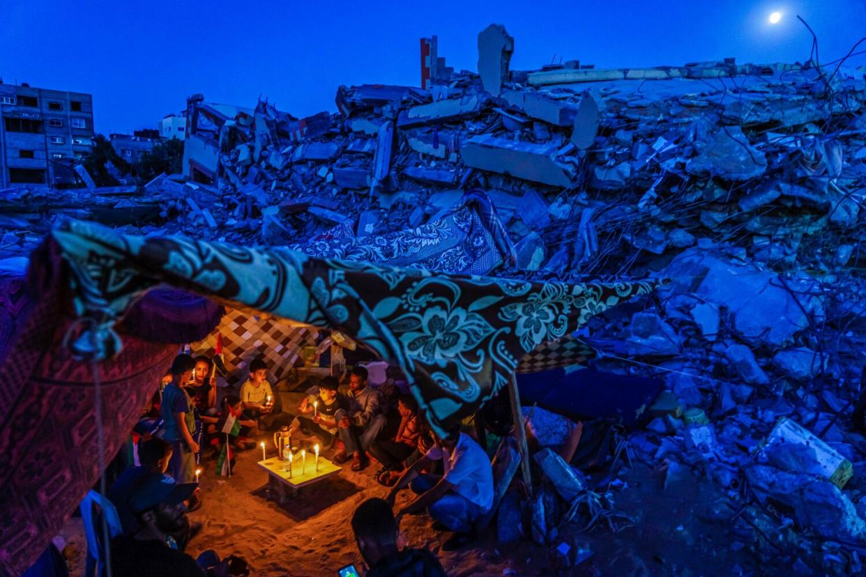 People sit by candles near destroyed buildings.