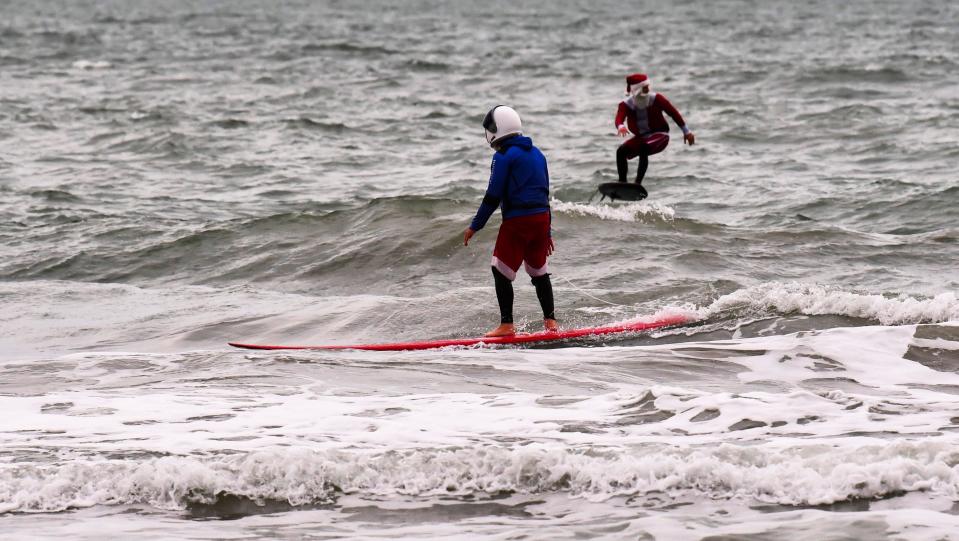 Bill Whiddon (foreground) rides his longboard wearing a Santa Claus suit beneath an astronaut costume while Gordon Harrison foil-surfs in the background during a Surfing Santas promotional photo shoot Tuesday south of Cocoa Beach.