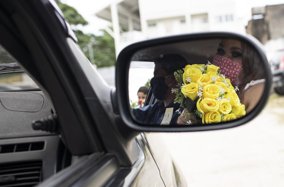 A bride is reflected on a car rearview window as she holds her bouquet after her drive-thru wedding at the neighborhood of Santa Cruz in Rio de Janeiro, Brazil, Thursday, May 28, 2020. Couples unable to have a traditional wedding because of the coronavirus pandemic are now taking part in drive-thru weddings. (AP Photo/Silvia Izquierdo)