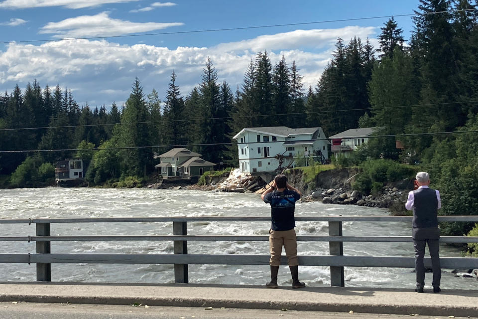 People pause on a bridge over the swollen Mendenhall River in Juneau, Alaska, on Sunday, Aug. 6, 2023, for a closer look or photos after a glacial dam burst earlier in the weekend caused flooding along the river and Mendenhall Lake. The city said at least two buildings were destroyed. (AP Photo/Becky Bohrer)