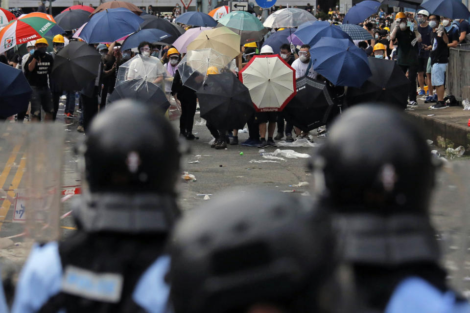 In this photo taken on Wednesday, June 12, 2019, protestors wear masks and helmets and hold umbrellas to protect their identities and provide cover from tear gas and pepper spray, as they clash with police near the Legislative Council in Hong Kong. Young Hong Kong residents protesting a proposed extradition law that would allow suspects to be sent to China for trial are seeking to safeguard their identities from potential retaliation by authorities employing mass data collection and sophisticated facial recognition technology. (AP Photo/Kin Cheung)