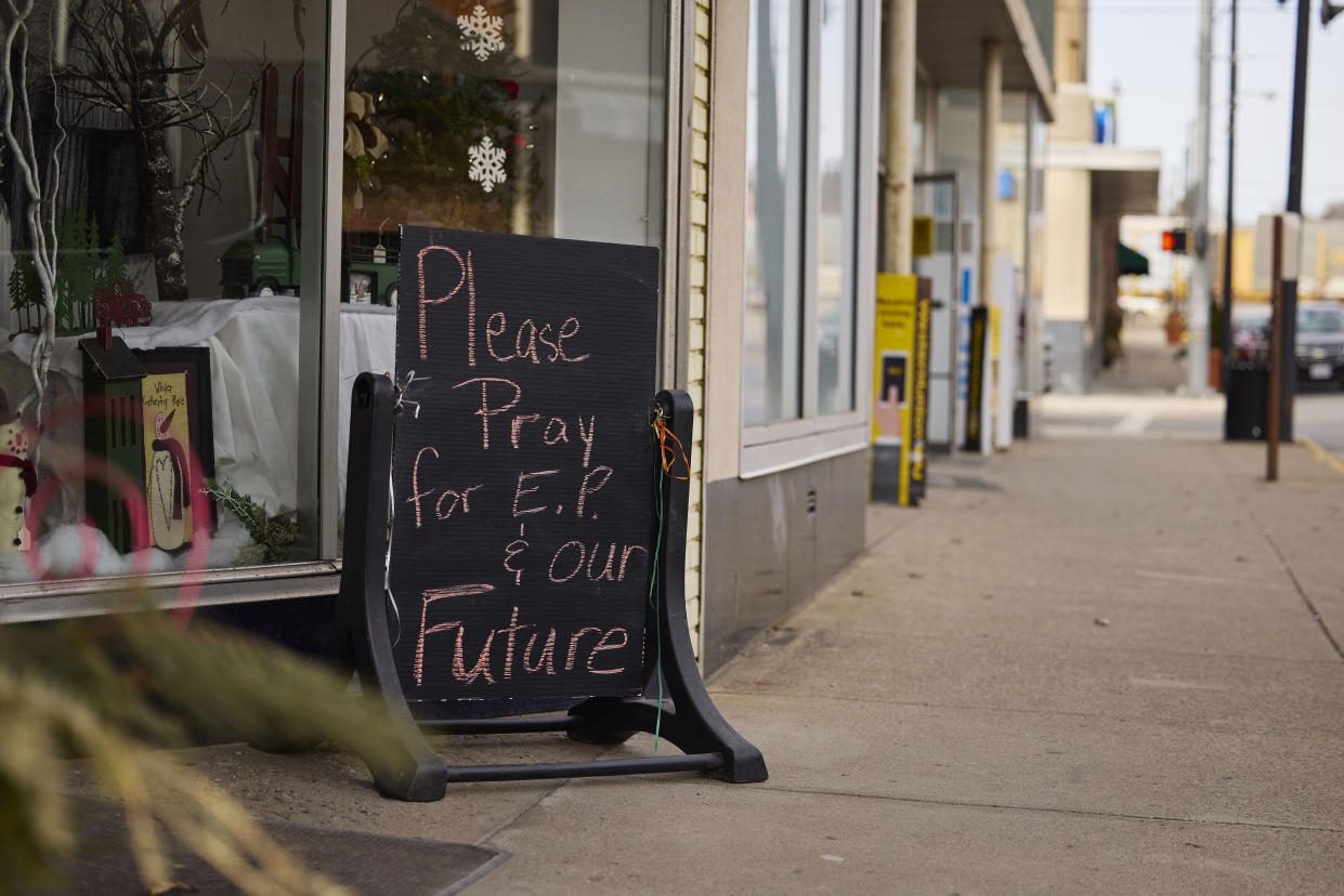 A handwritten sign on a town sidewalk says: Please Pray for E.P.  & our Future.
