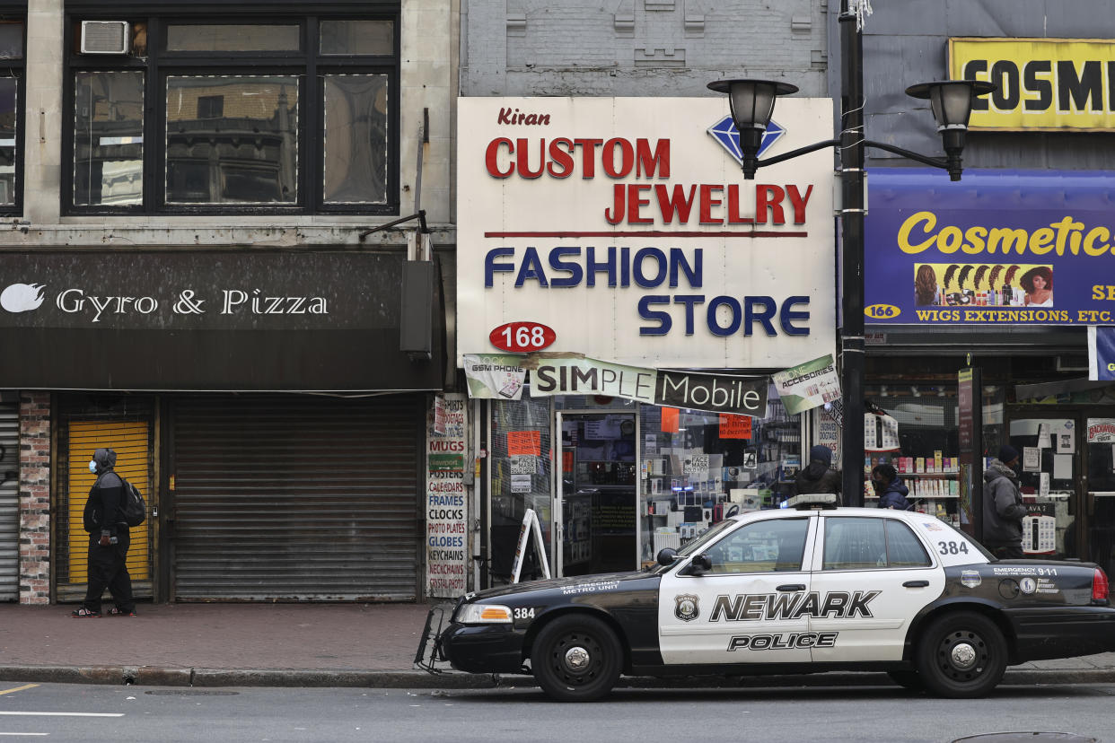 A vehicle marked Newark Police in front of a store with a sign saying Kiran Custom Jewelry, Fashion Store and Simple Mobile. The adjacent stores say Gyro & Pizza and Cosmetic, Wigs Extensions.