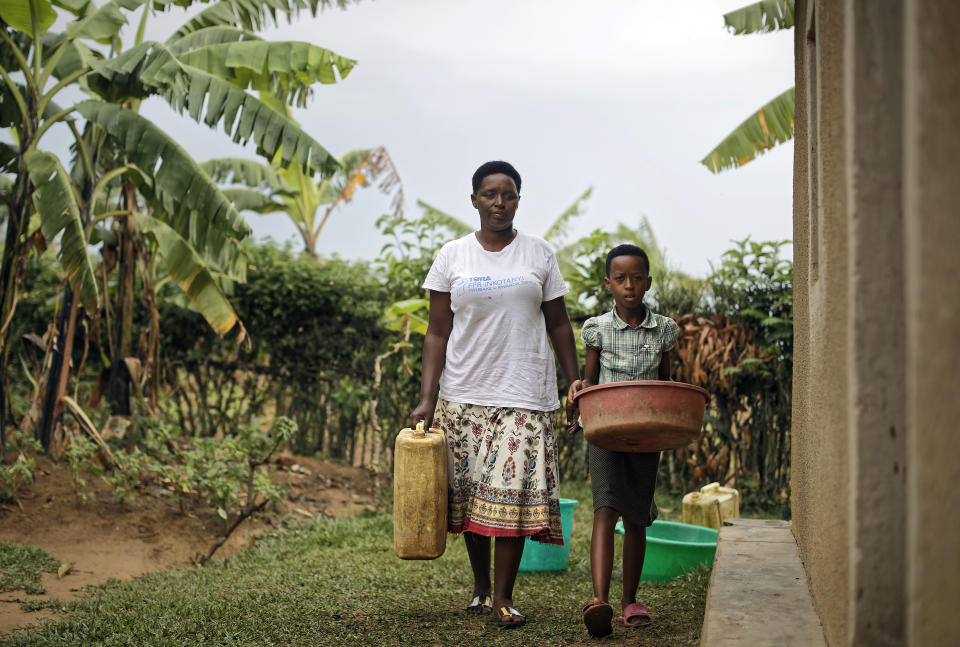 In this photo taken Thursday, April 4, 2019, genocide survivor Jannette Mukabyagaju, 42, and her 8-year-old daughter Natasha Umutesi bring buckets of rainwater collected during a rainstorm in to their home in the reconciliation village of Mbyo, near Nyamata, in Rwanda. Twenty-five years after the genocide the country has six "reconciliation villages" where convicted perpetrators who have been released from prison after publicly apologizing for their crimes live side by side with genocide survivors who have professed forgiveness. (AP Photo/Ben Curtis)