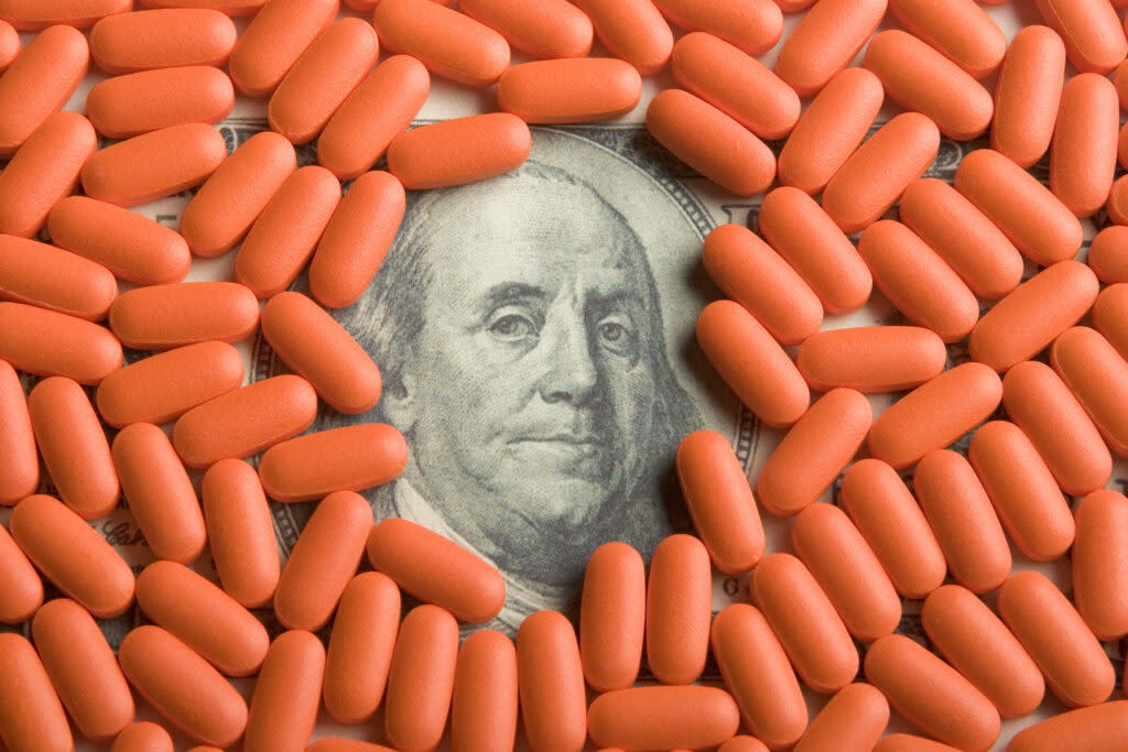 Photo illustration with $100 bill covered by prescription pills