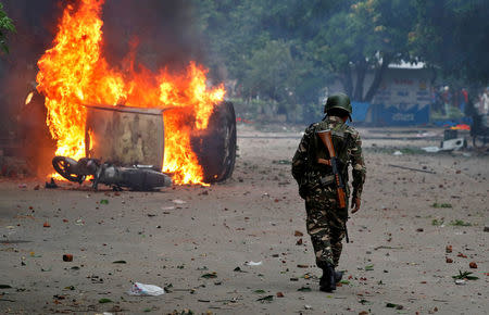 A member of the security forces walks towards a burning vehicles during violence in Panchkula, India, August 25, 2017. REUTERS/Cathal McNaughton