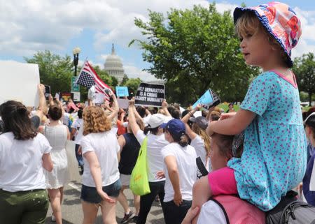 A child sits atop the shoulders of a demonstrator as hundreds of women and immigration activists march to the U.S. Capitol as part of a rally calling for "an end to family detention" and in opposition to the immigration policies of the Trump administration, in Washington, U.S., June 28, 2018. REUTERS/Jonathan Ernst