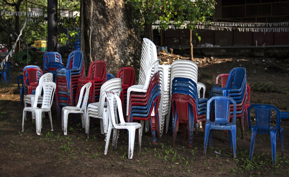 Chairs that were used for an open air meeting lie stacked beneath a roadside tree in Kochi, Kerala state, India, Thursday, April 22, 2021. The government has revised the guidelines on public gatherings following the spike in coronavirus cases. (AP Photo/R S Iyer)