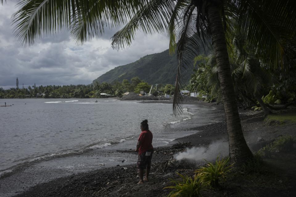A person burns fallen leaves on a beach in Teahupo'o, Tahiti, French Polynesia, Friday, Jan. 13, 2024. The decision to host part of the Olympic Games here has thrust unprecedented challenges onto a small community that has long cherished and strives to protect a way of life. (AP Photo/Daniel Cole)