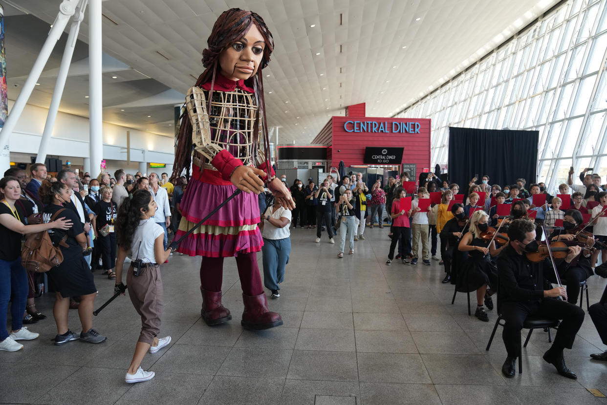 La Pequeña Amal y sus titiriteros recorren la Terminal 4 del Aeropuerto Internacional Kennedy, el miércoles 14 de septiembre de 2022, cuando los recibieron miembros de la Orquesta de la Ópera Metropolitana y su coro de niños. (Todd Heisler/The New York Times)
