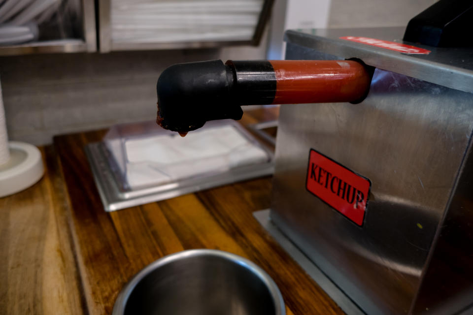 A ketchup pump dispenser with the label "KETCHUP" on it, positioned over a stainless steel container