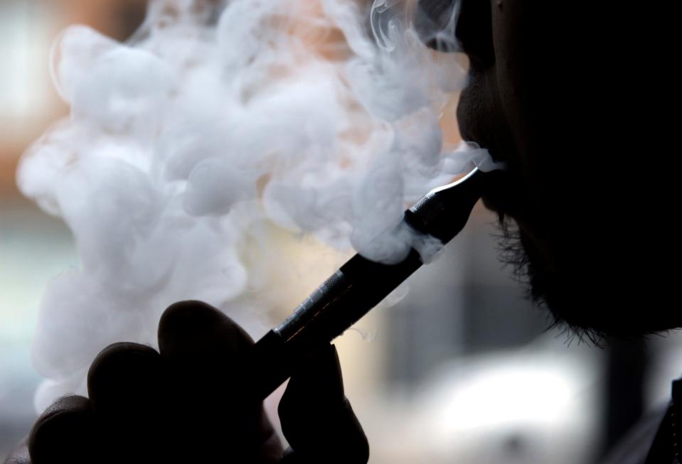 In this 2014 file photo, a man smokes an electronic cigarette in Chicago. Major Leader Mitch McConneell said April18,2019 that he will introduce a bill to raise the age for buying cigarette or vaping products to 21.