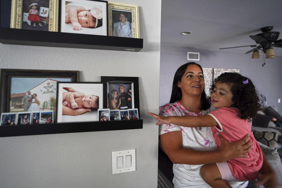 Laura Guerra and her daughter Emilia, 2, look at her father's pictures at their home in Riverside, Calif., on Monday, July 11, 2022. For now, Laura is focused on making sure her daughter, Emilia, remembers her father. Rigo Guerra passed away on Dec. 24, 2020, due to complications following a monthlong battle with COVID-19. California has approved trust funds for some children from low-income families who lost a parent or caregiver to COVID-19. The Legislature set aside $100 million in the state budget to put into trust funds. (AP Photo/Damian Dovarganes)