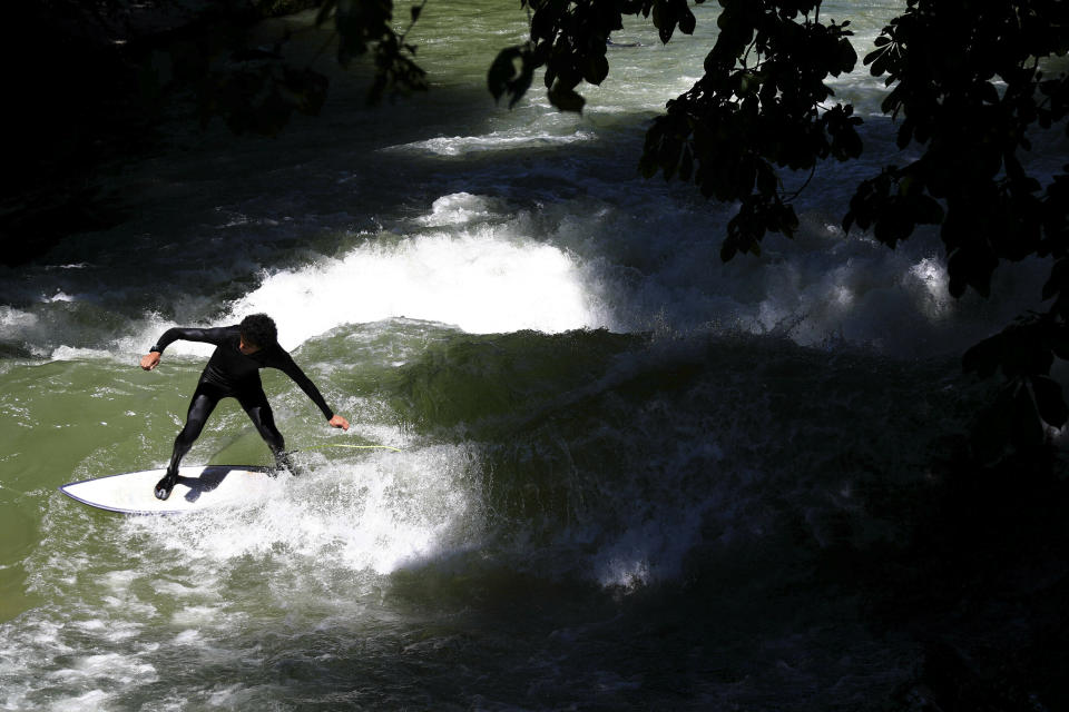 A surfer rides an artificial wave in the river "Eisbach" at the English Garden downtown in Munich, Germany, Monday, June 24, 2019. (AP Photo/Matthias Schrader)