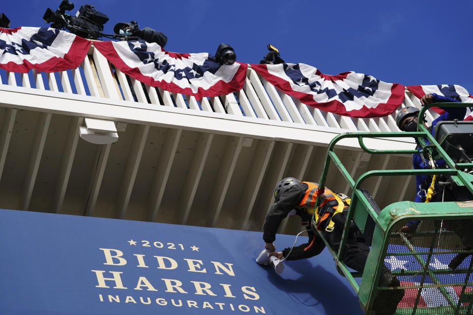 Unos trabajadores instalan unos banderines afuera de la Casa Blanca el lunes 18 de enero de 2021, en Washington, durante los preparativos para la ceremonia de investidura del presidente electo Joe Biden y de la vicepresidenta electa Kamala Harris. (AP Foto/John Minchillo)