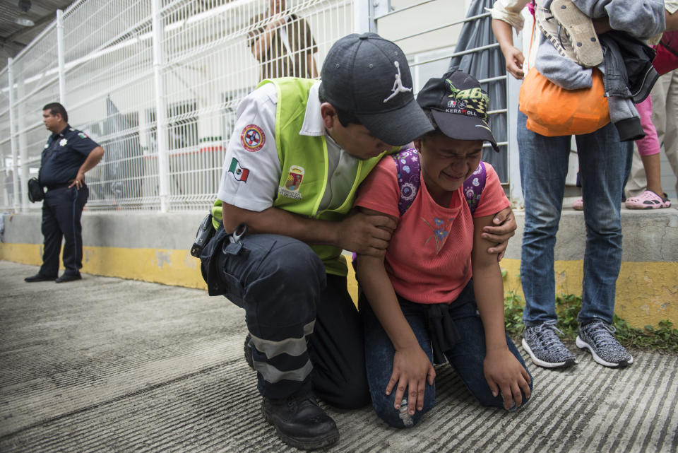 A Honduras migrant is comforted by a Mexican paramedic after her mother fainted while crossing the border between Guatemala and Mexico, in Ciudad Hidalgo, Mexico, Saturday, Oct. 20, 2018. Mexican officials are refusing to yield to demands from the caravan of Central American migrants that they be allowed to enter the country en masse but announced they would hand out numbers to those waiting to cross and allow them to enter in small groups. (AP Photo/Oliver de Ros)