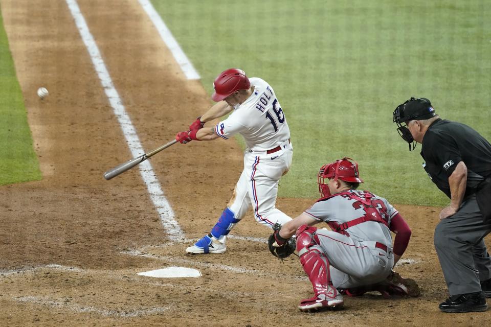 Texas Rangers' Brock Holt, left, connects for a run-scoring sacrifice fly in the seventh inning of a baseball game as Los Angeles Angels' Max Stassi, center, and umpire Joe West, right, look on in Arlington, Texas, Monday, Aug. 2, 2021. (AP Photo/Tony Gutierrez)