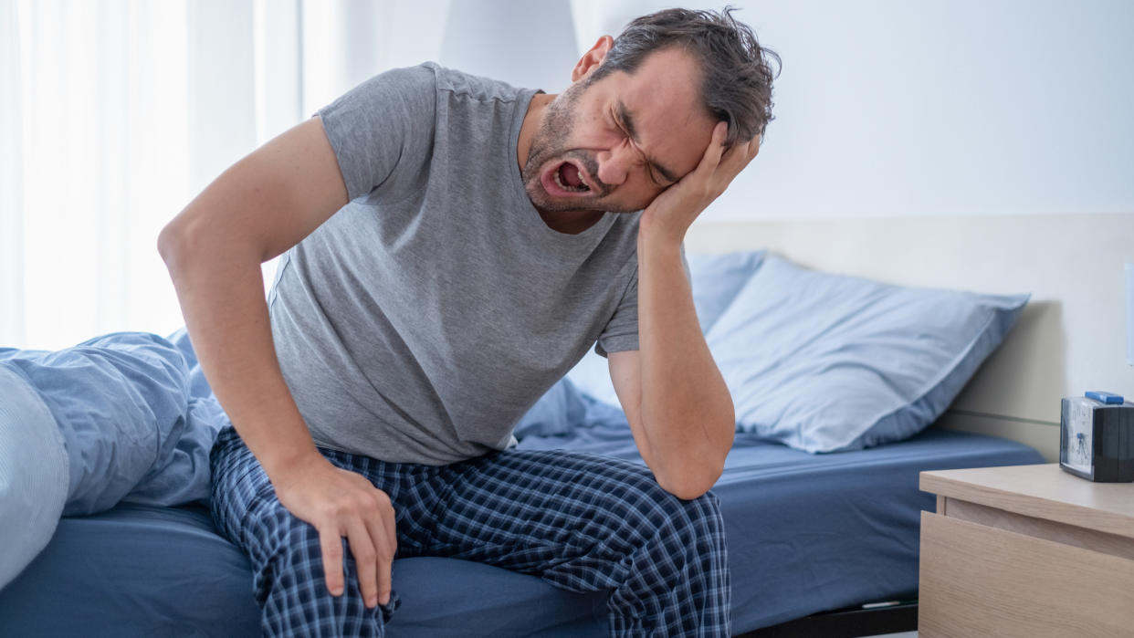  A man sits up in bed at night because restless leg syndrome is keeping him awake and is affecting his sleep. 