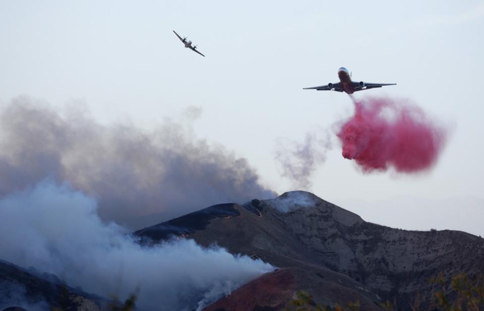 A fire spotter plane peels off after marking the drop location for an air tanker, which drops a cloud of pink retardant.