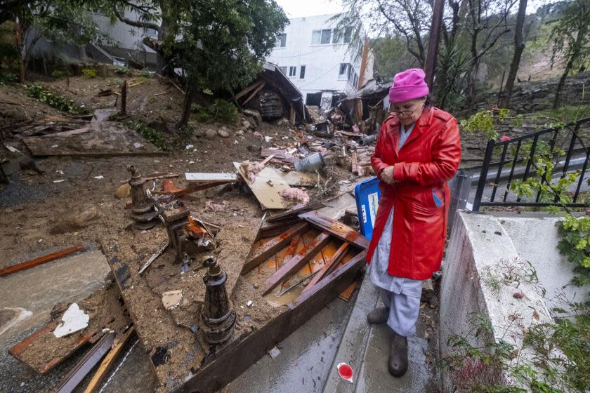 Los Angeles, CA - February 05: A resident walks by a home is damaged by a storm near Caribou Ln during a rainstorm at Hollywood Hills on Monday, Feb. 5, 2024 in Los Angeles, CA. (Ringo Chiu / For The Times)