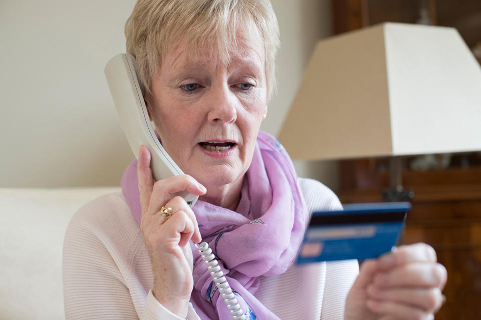 Elderly woman holds up credit card and speaks on landline phone