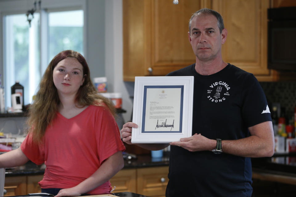 In this May 22, 2020, photo, Jason Nixon, right, holds a letter from President Donald Trump as he poses with his daughter, Morgan, left, as they display memorabilia from last year's shooting that took the life of Kate Nixon at their home in Virginia Beach, Va. As the shooting's one-year anniversary approaches this weekend, some of the victim's family members say the rampage is effectively forgotten. (AP Photo/Steve Helber)