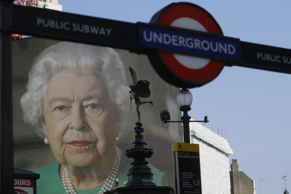 FILE - In this April 9, 2020 file photo an image of Britain's Queen Elizabeth II and quotes from her historic television broadcast commenting on the coronavirus pandemic are displayed on a big screen behind the Eros statue and a London underground train station entrance sign at Piccadilly Circus in London. Queen Elizabeth II, Britain’s longest-reigning monarch and a rock of stability across much of a turbulent century, has died. She was 96. Buckingham Palace made the announcement in a statement on Thursday Sept. 8, 2022. (AP Photo/Kirsty Wigglesworth, File)