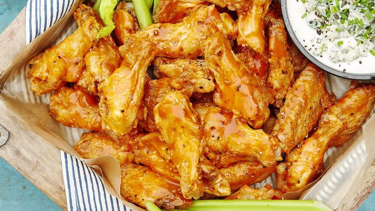 spicy oven baked wings on a wooden serving tray with celery sticks and a small bowl of blue cheese dip